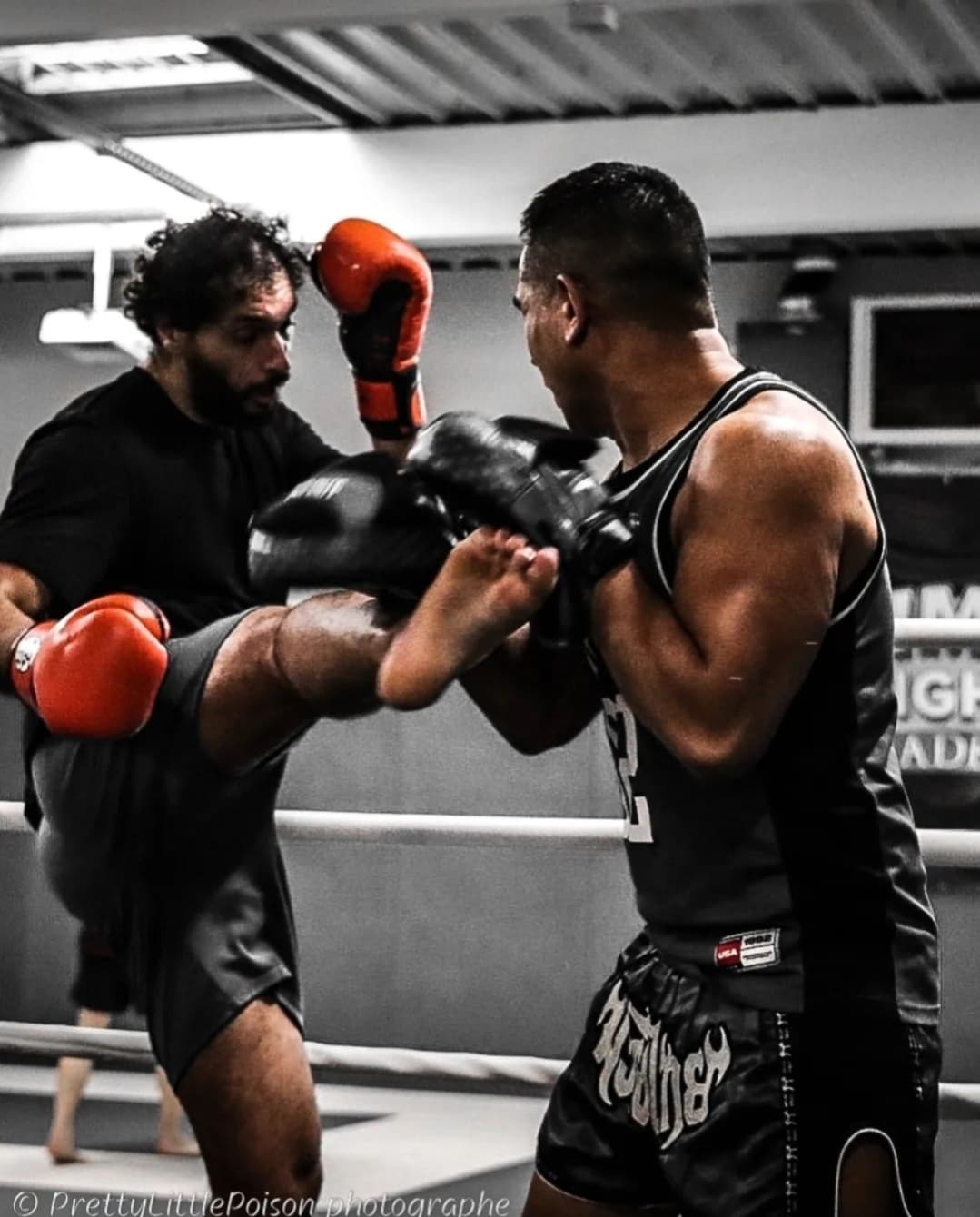 Un combattant effectue un coup de pied circulaire au corps de son partenaire qui se protège dans un ring de Muay Thaï.